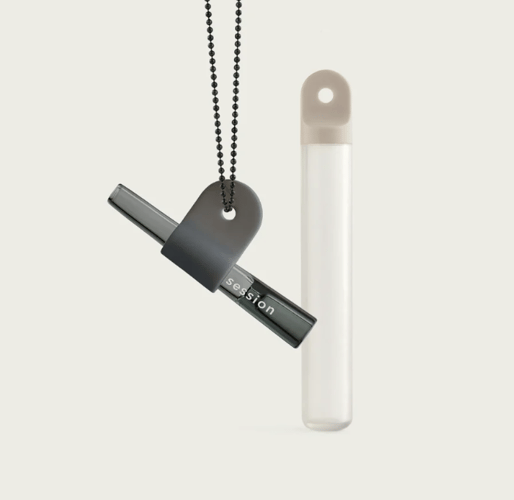 A grey glass one-hitter is help by a grey silicon tab attached to a ball chain neckless. The background is off white and there is a clear stash tube with an off white top standing upright.
