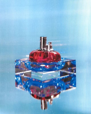 An Edie Parker Glass Tabletop lighter. The lighter part is red, and it sits in the center of a reflective blue ashtray.