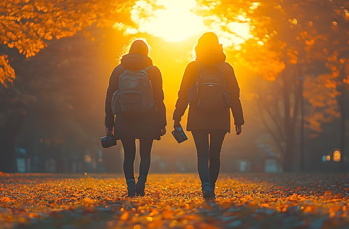 Two people walking away from the camera in a golden autumn light. They are surrounded by fall colors, and walk on fallen leaves.